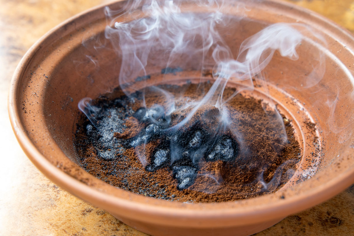 Burning coffee grounds for mosquito and wasp repellent in clay bowl producing burned coffee smoke for banishing insects