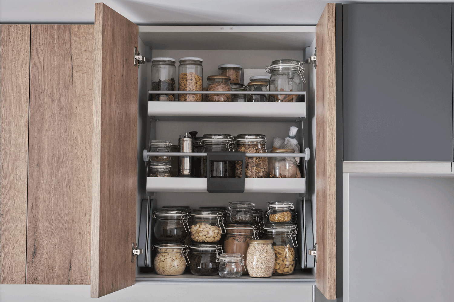 Variety of dry foods, grains, nuts, cereals in glass jars in kitchen cupboard. Zero waste storage concept.