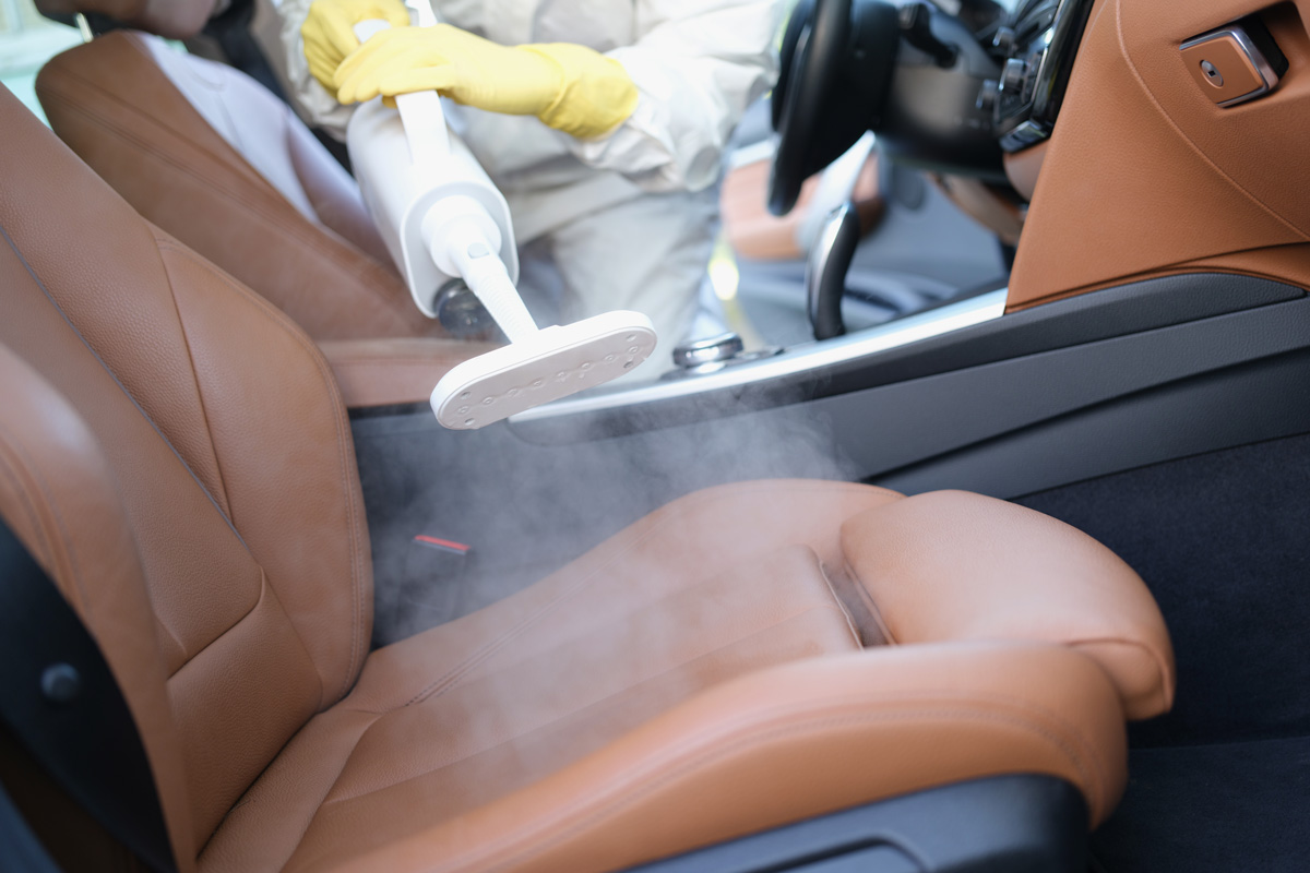 A specialist cleans a car interior with a steam cleaner